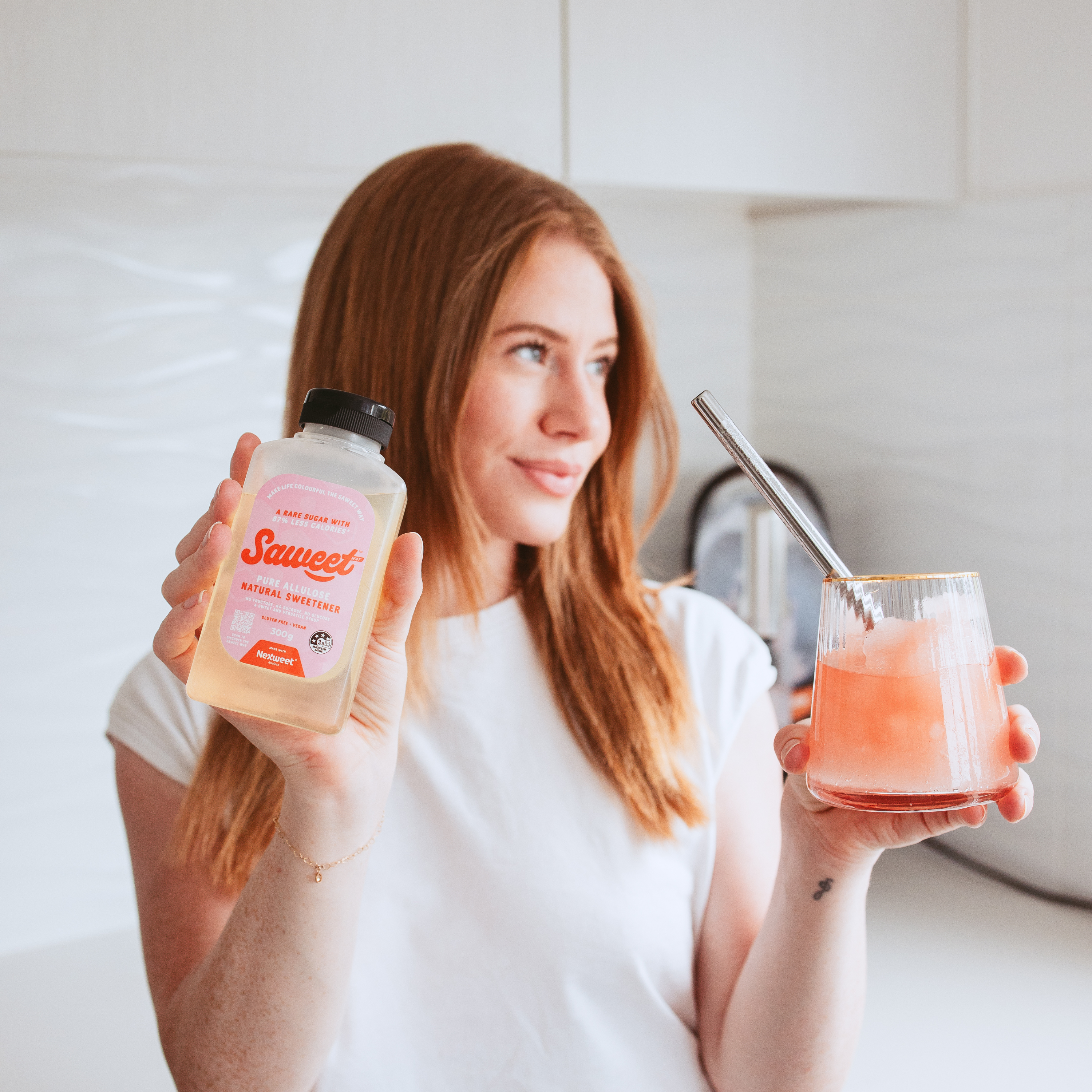 Woman holding Saweet Way pure allulose natural sweetener and a pink iced drink, showing an easy low calorie sugar swap for everyday beverages.
