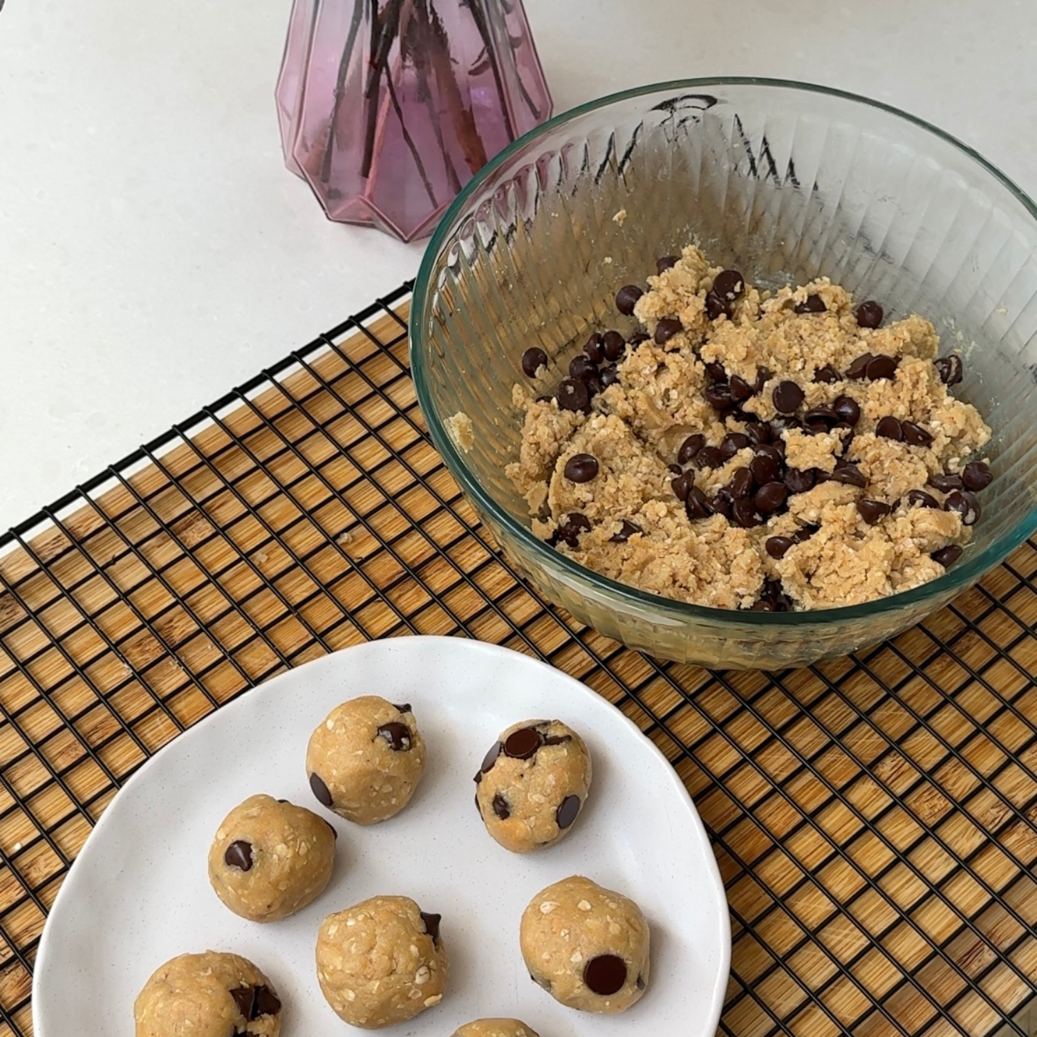 A plate of rolled chocolate chip protein cookie dough balls made with SaweetWay allulose, styled alongside a bowl of the raw cookie dough mixture