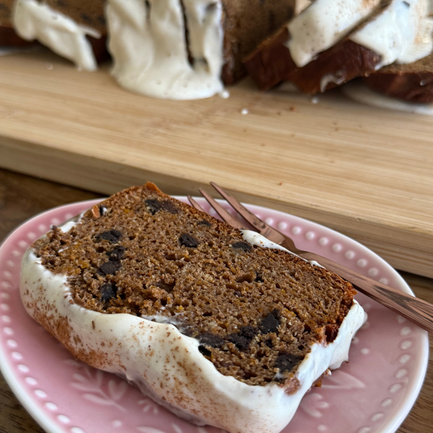 A slice of chocolate chip spiced pumpkin loaf baked with SaweetWay allulose served on a plate with a fork, with the full loaf visible in the background