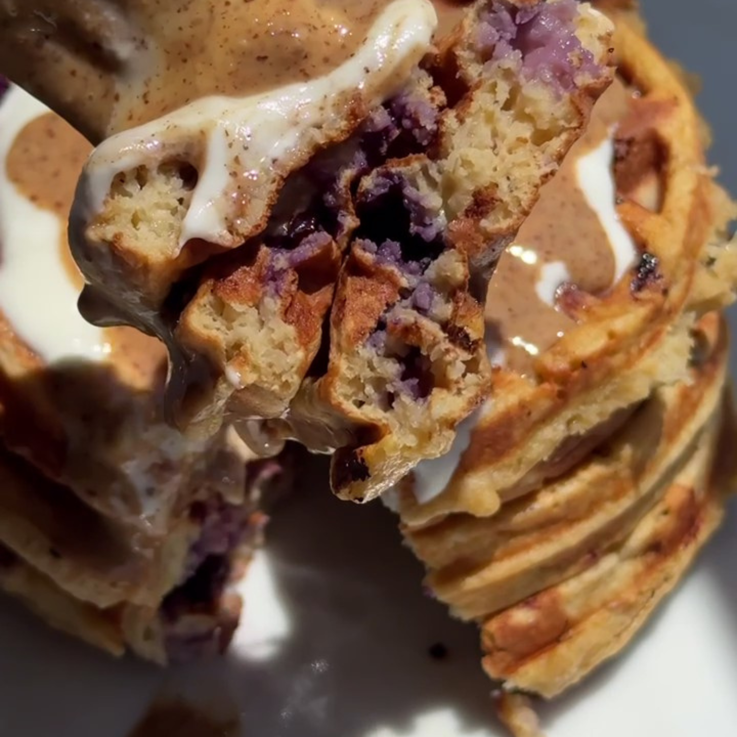 A stack of golden collagen blueberry waffles made with SaweetWay allulose, with a forkful of waffle cut out and held up alongside the stack